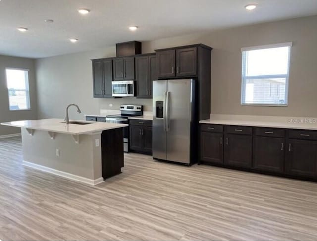 kitchen with sink, a breakfast bar area, a center island with sink, light hardwood / wood-style flooring, and appliances with stainless steel finishes