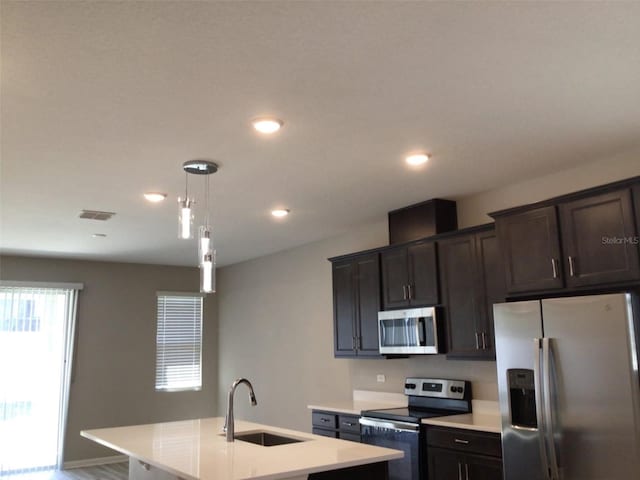 kitchen with dark brown cabinetry, sink, decorative light fixtures, stainless steel appliances, and a kitchen island with sink