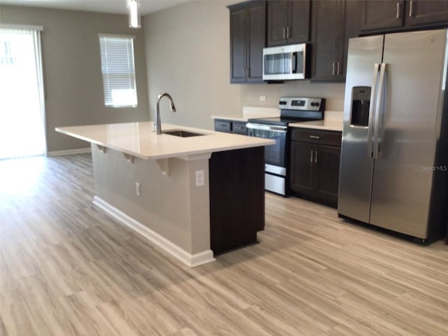 kitchen featuring appliances with stainless steel finishes, sink, a center island with sink, and light wood-type flooring