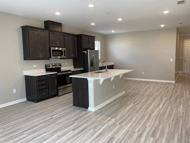 kitchen with appliances with stainless steel finishes, sink, light hardwood / wood-style floors, and an island with sink