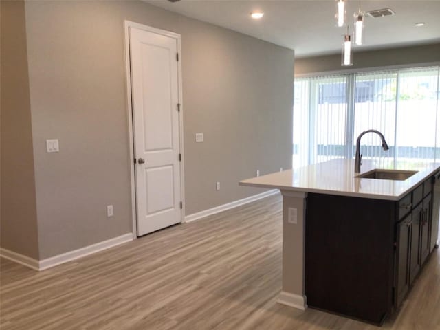 kitchen featuring pendant lighting, sink, light hardwood / wood-style flooring, and a center island with sink