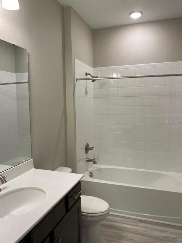 full bathroom with vanity, tiled shower / bath, hardwood / wood-style floors, and toilet