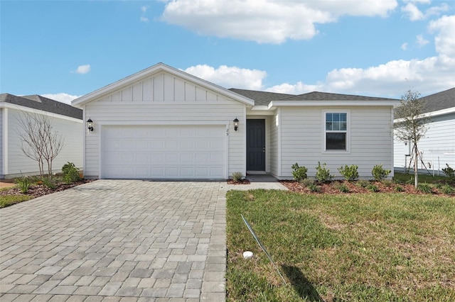 single story home featuring an attached garage, decorative driveway, board and batten siding, and a front yard