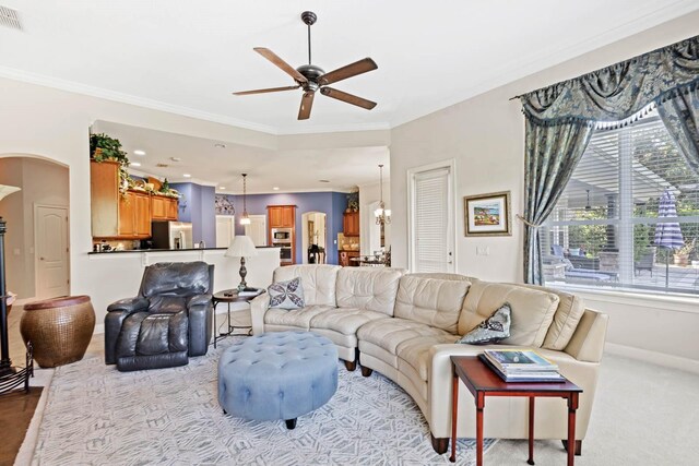 living room with ceiling fan with notable chandelier, crown molding, and light colored carpet