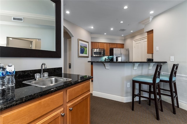 kitchen featuring sink, appliances with stainless steel finishes, a kitchen breakfast bar, dark carpet, and dark stone counters