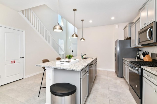 kitchen with appliances with stainless steel finishes, gray cabinets, light tile patterned floors, a kitchen island with sink, and light stone countertops