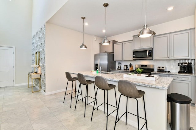 kitchen featuring gray cabinetry, appliances with stainless steel finishes, decorative light fixtures, and a kitchen island with sink