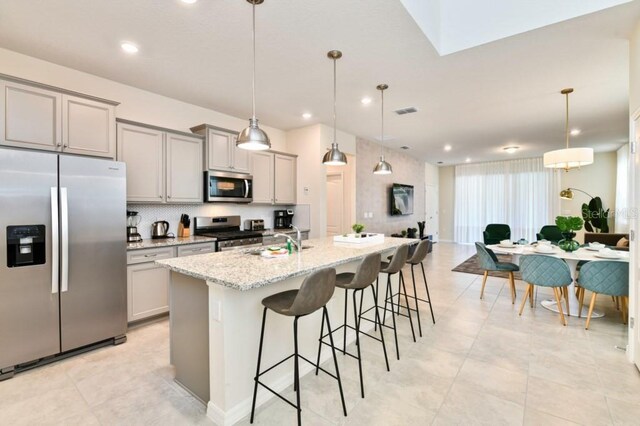 kitchen featuring decorative light fixtures, sink, appliances with stainless steel finishes, light tile patterned floors, and a kitchen island with sink