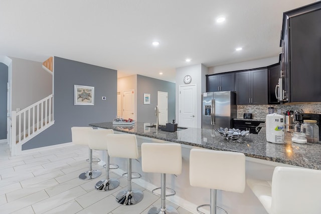 kitchen with sink, dark stone counters, stainless steel fridge with ice dispenser, and backsplash