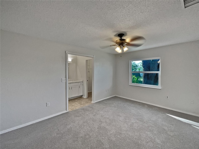 unfurnished bedroom with ceiling fan, light colored carpet, a textured ceiling, and ensuite bath