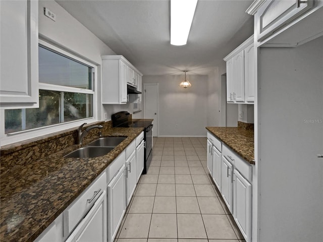 kitchen with black range with electric stovetop, sink, light tile patterned floors, dark stone countertops, and white cabinetry