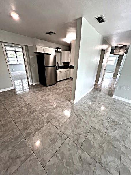 kitchen with sink, stainless steel refrigerator, white cabinets, and light tile patterned floors