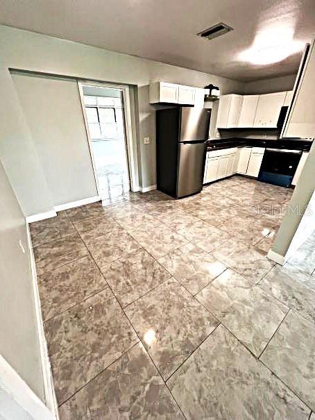 kitchen with stainless steel fridge, white cabinetry, and light tile patterned floors