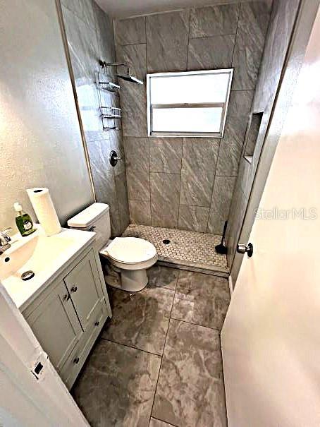 bathroom featuring tiled shower, tile patterned floors, toilet, and vanity