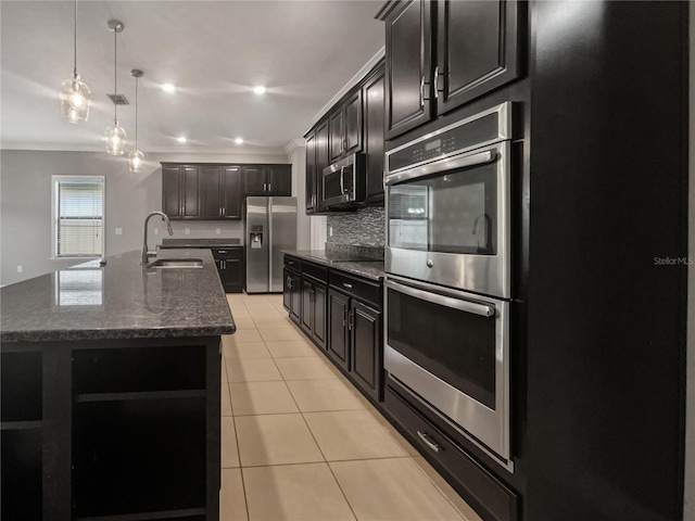 kitchen with decorative light fixtures, tasteful backsplash, stainless steel appliances, sink, and a kitchen island with sink