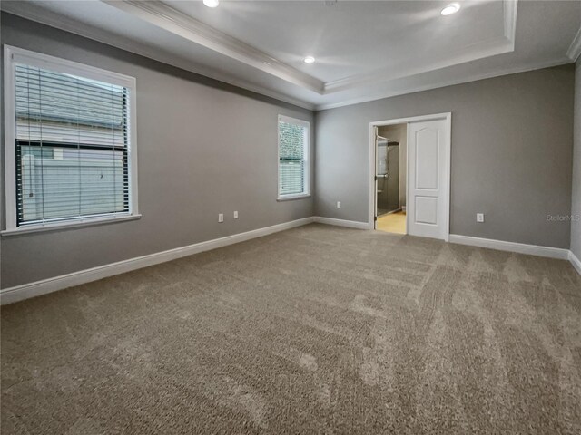 unfurnished bedroom featuring a raised ceiling, crown molding, ensuite bath, and carpet floors