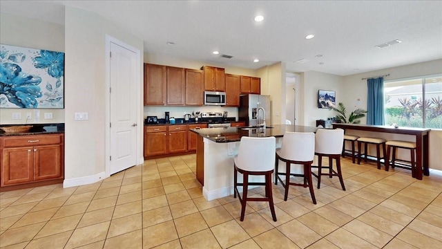 kitchen with a kitchen bar, appliances with stainless steel finishes, light tile patterned flooring, and a center island with sink