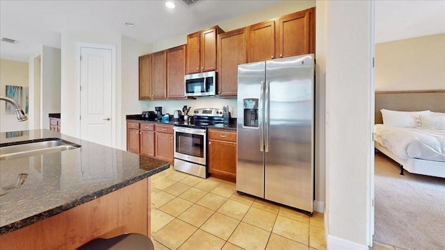 kitchen with sink, light carpet, stainless steel appliances, and dark stone countertops