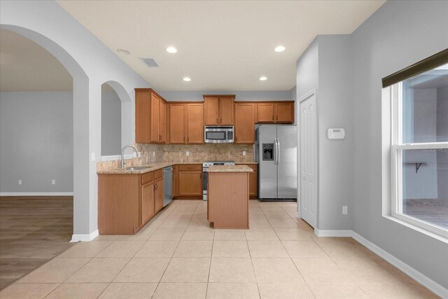 kitchen with light stone counters, tasteful backsplash, a center island, and appliances with stainless steel finishes