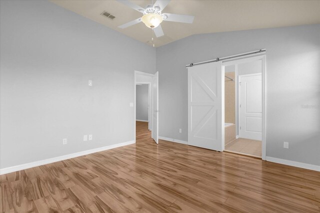 unfurnished bedroom featuring ensuite bathroom, lofted ceiling, light wood-type flooring, ceiling fan, and a barn door