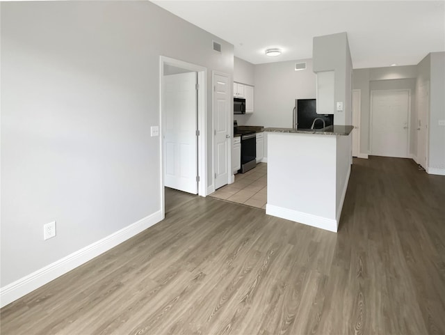 kitchen featuring black appliances, white cabinetry, dark stone counters, light hardwood / wood-style floors, and kitchen peninsula