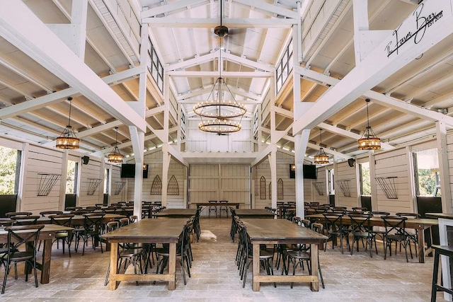 dining area with high vaulted ceiling, plenty of natural light, wood walls, and a chandelier