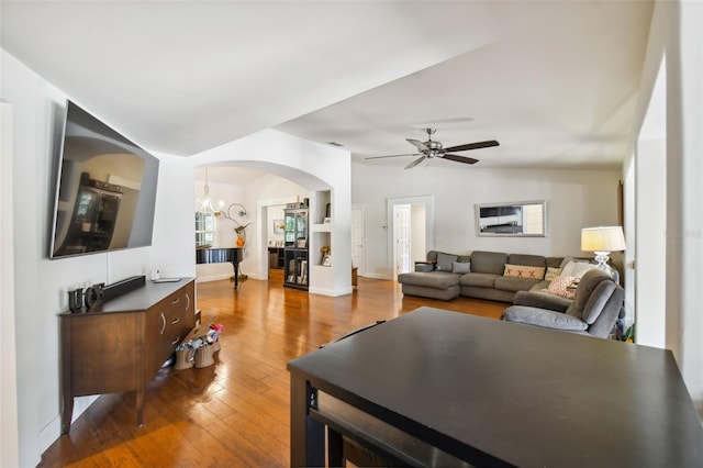 living room featuring lofted ceiling, ceiling fan with notable chandelier, dark hardwood / wood-style floors, and built in shelves