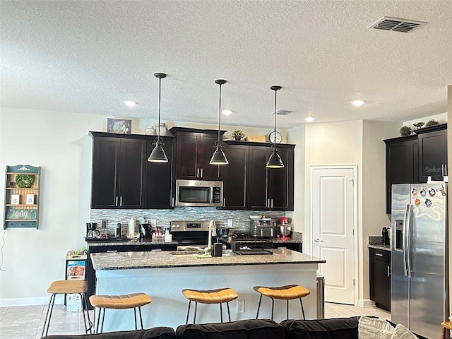 kitchen featuring a center island with sink, appliances with stainless steel finishes, a kitchen breakfast bar, pendant lighting, and backsplash