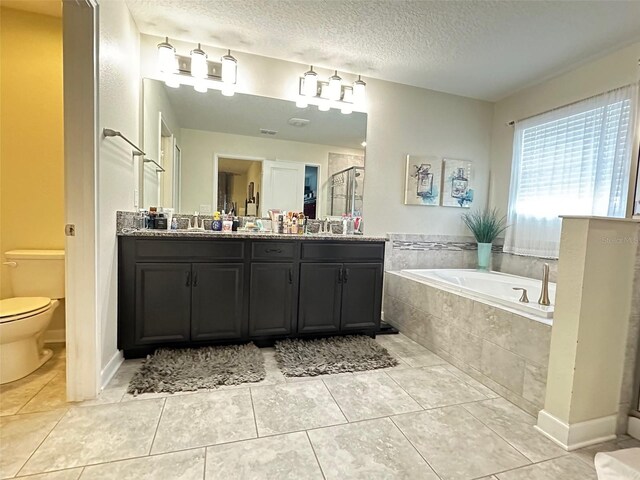 bathroom featuring tile patterned floors, tiled tub, dual vanity, toilet, and a textured ceiling