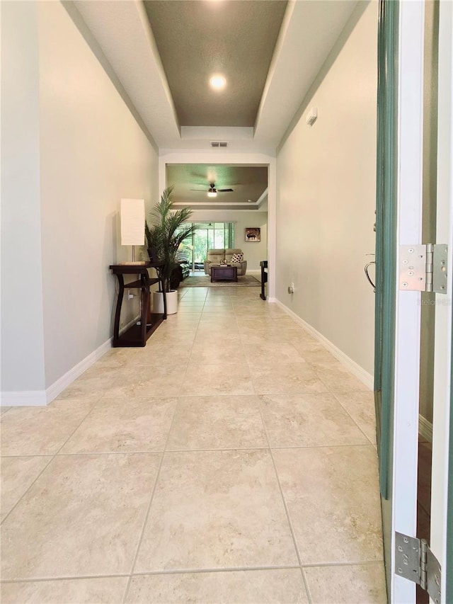 hall with light tile patterned floors and a tray ceiling