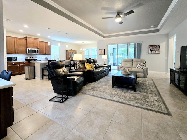 living room with light tile patterned flooring, ceiling fan with notable chandelier, ornamental molding, a raised ceiling, and a textured ceiling