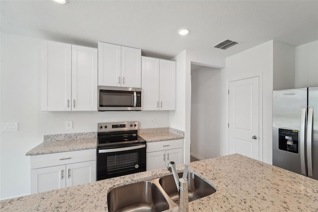 kitchen with appliances with stainless steel finishes, white cabinetry, light stone counters, and sink