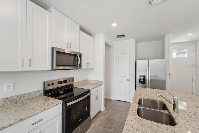 kitchen featuring appliances with stainless steel finishes, white cabinets, light stone countertops, and sink