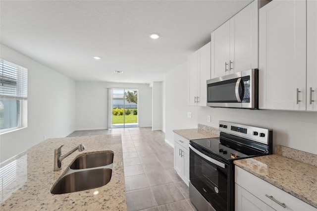 kitchen featuring appliances with stainless steel finishes, light stone countertops, white cabinets, light tile patterned flooring, and sink