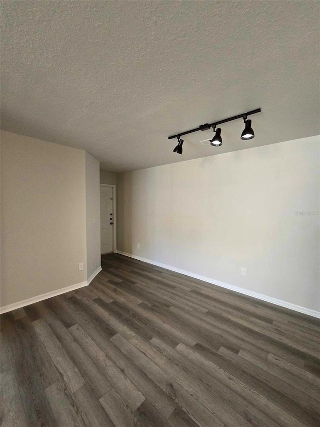 unfurnished room featuring rail lighting, a textured ceiling, and dark hardwood / wood-style floors