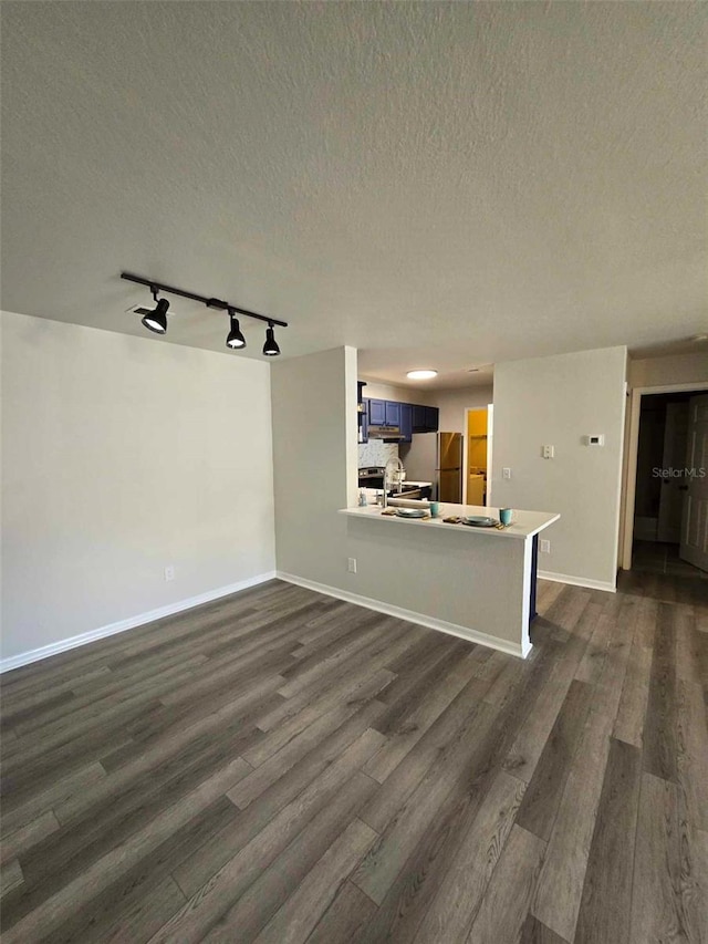 unfurnished living room featuring dark wood-type flooring, rail lighting, a textured ceiling, and sink