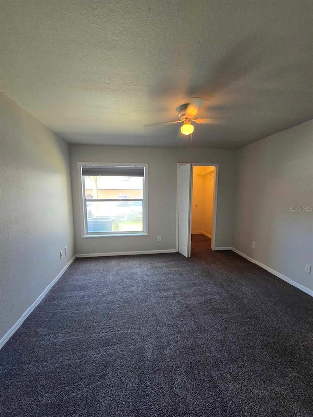 spare room featuring ceiling fan, dark carpet, and a textured ceiling