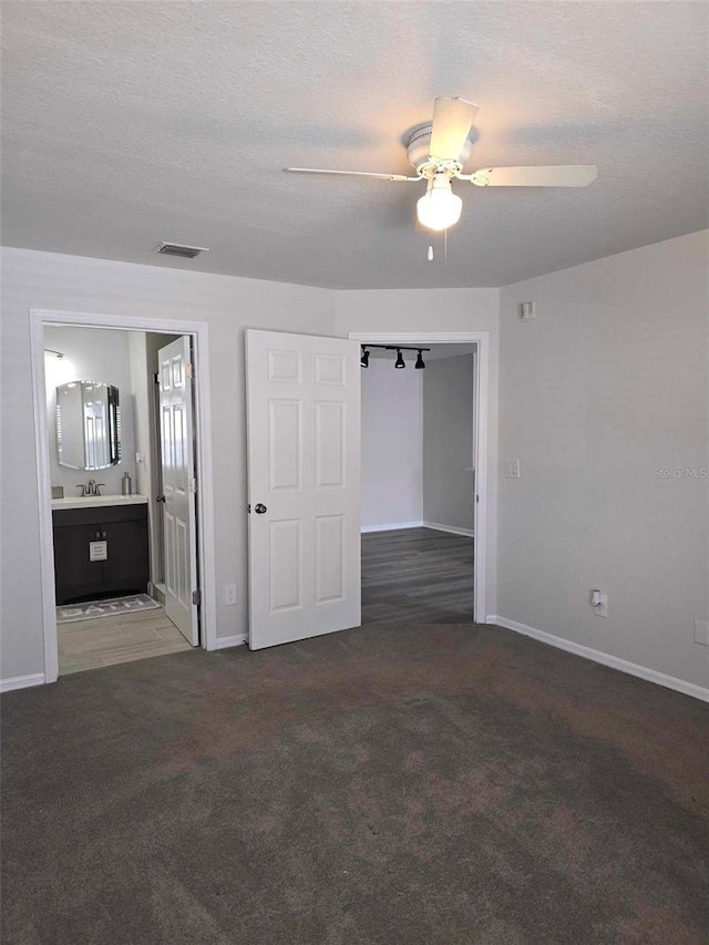 unfurnished bedroom featuring a textured ceiling, connected bathroom, dark colored carpet, sink, and ceiling fan