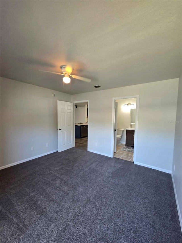 unfurnished bedroom featuring ceiling fan, dark carpet, ensuite bathroom, and a textured ceiling