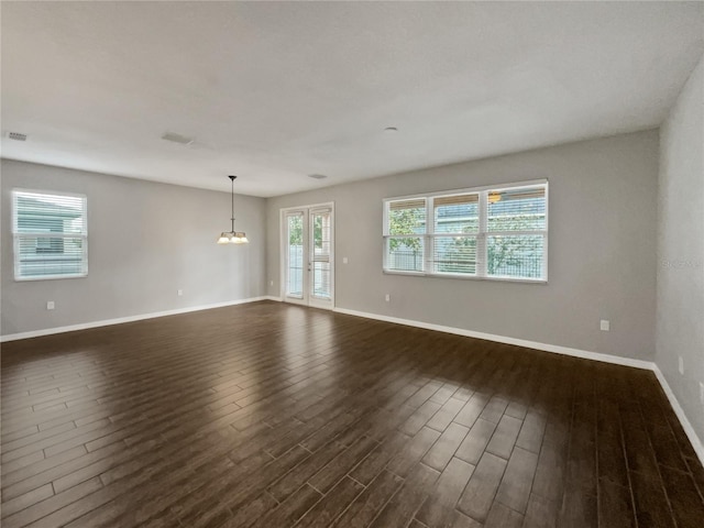 spare room with a notable chandelier and dark wood-type flooring