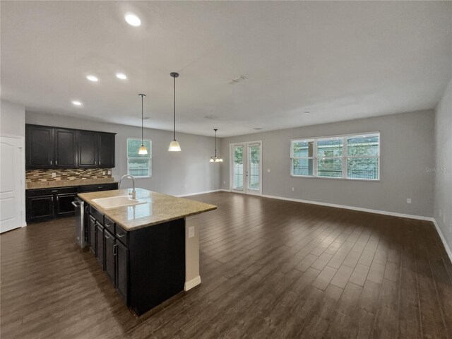 kitchen featuring dark hardwood / wood-style floors, decorative light fixtures, tasteful backsplash, sink, and a center island with sink