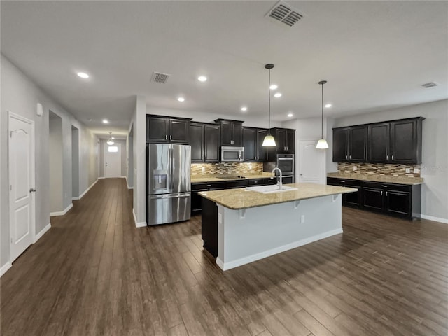 kitchen with appliances with stainless steel finishes, pendant lighting, an island with sink, a kitchen bar, and dark wood-type flooring