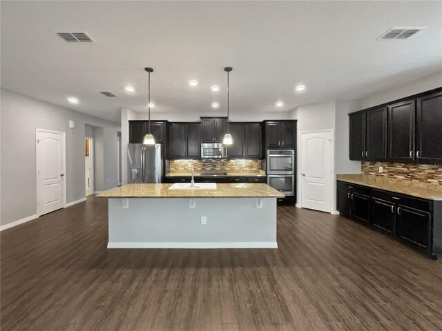 kitchen featuring sink, appliances with stainless steel finishes, dark hardwood / wood-style floors, pendant lighting, and a kitchen island with sink