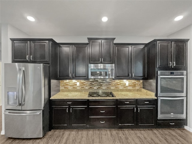 kitchen with tasteful backsplash, light stone counters, stainless steel appliances, and light wood-type flooring