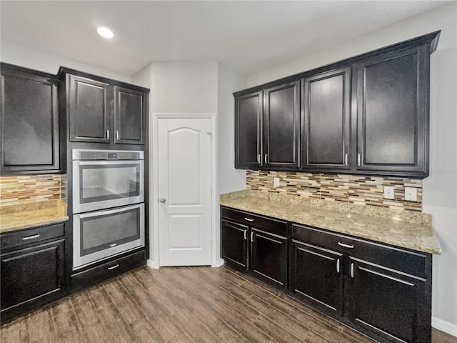 kitchen with tasteful backsplash, double oven, dark wood-type flooring, and light stone countertops