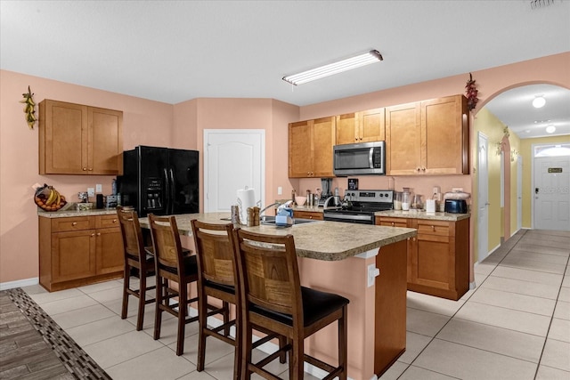 kitchen featuring a kitchen bar, appliances with stainless steel finishes, a center island with sink, and light tile patterned floors