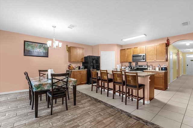 kitchen featuring a breakfast bar area, an inviting chandelier, appliances with stainless steel finishes, decorative light fixtures, and a center island with sink