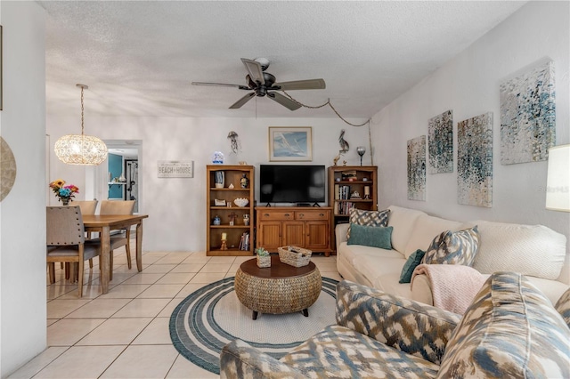 living room featuring a textured ceiling, light tile patterned floors, and ceiling fan with notable chandelier