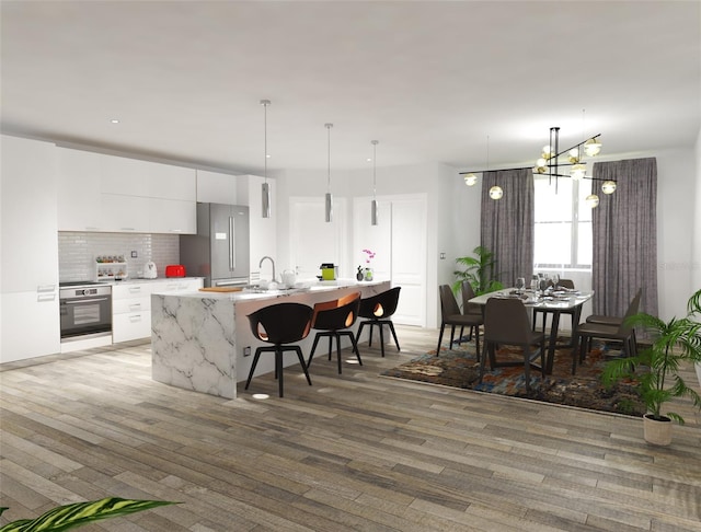 kitchen featuring light hardwood / wood-style flooring, white cabinetry, appliances with stainless steel finishes, pendant lighting, and a notable chandelier