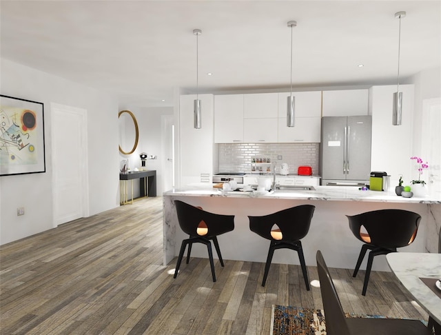 kitchen featuring hardwood / wood-style floors, a kitchen bar, white cabinetry, and stainless steel refrigerator